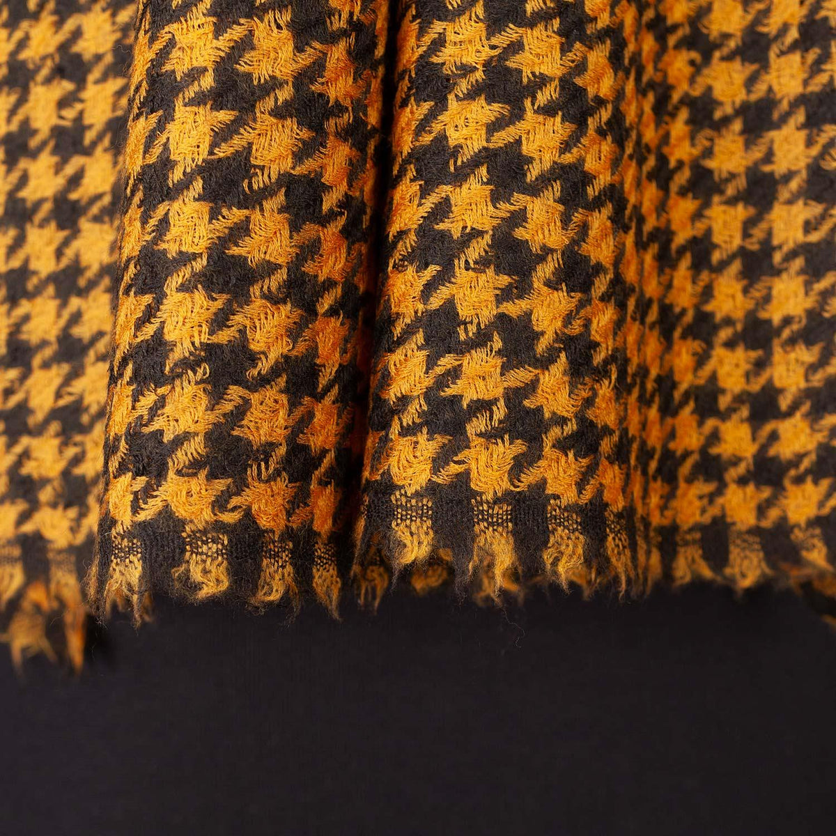 A close-up detailing the luxurious golden yellow and black hand-dyed Houndstooth pattern with a soft fringed edge. Made in India.