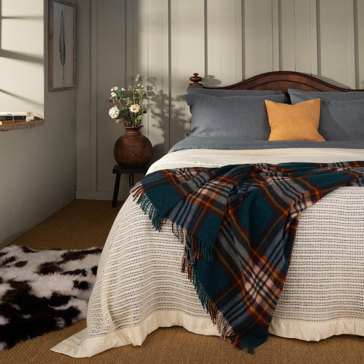 Crafted from traditional Shetland wool featuring a n authentic tartan check, this richly coloured throw in classic teal, burnt orange and cream is shown draped on the end of a bed. 140 x 185 CMS including tassels.