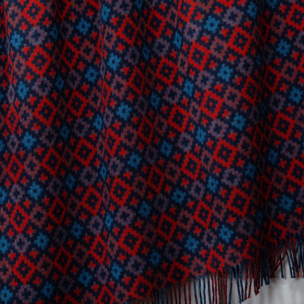 A close-up detailing  the geometric diamond pattern of navy, teal and burnt orange. Made in the UK. 100% Shetland Wool.
