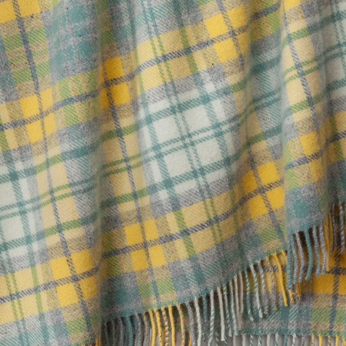 Close-up of the tartan wool throw in sun-kissed blends of light yellow, soft grey and white. 100% Pure New Wool. Made in Britain.