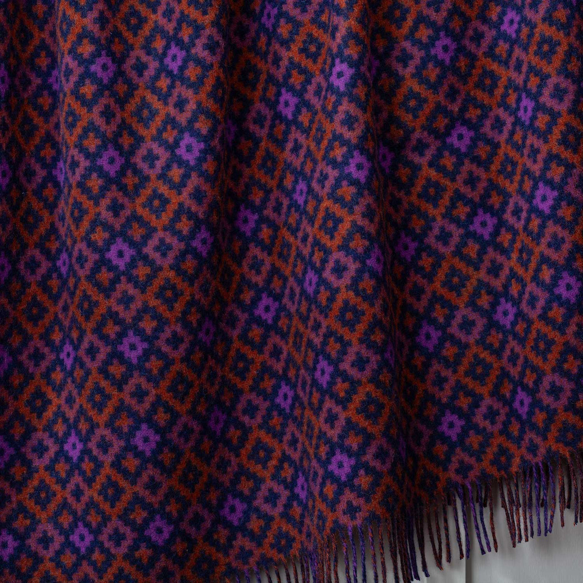 A close-up detailing  the geometric diamond pattern of orange, purple, navy and brown. Made in the UK. 100% Shetland Wool.