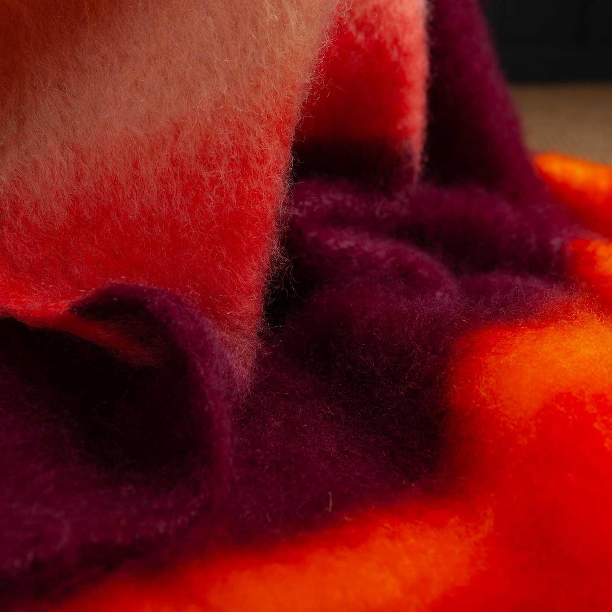 A close-up of the Festival Mohair Blanket Tango, detailing the bands of warm reds, pinks and oranges. 50% Mohair, 48% Wool, 2% Polyamide.