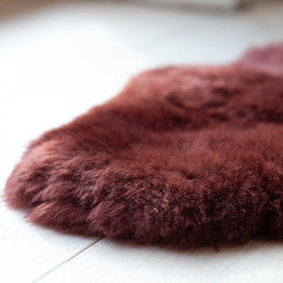 Sheepskin rug in Autumn reddish brown, close-up photo on wooden floor boards.
