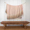 Lambswool throw hung over a line, pink and light camel brown tones with a diamond pattern, long cream tassels.