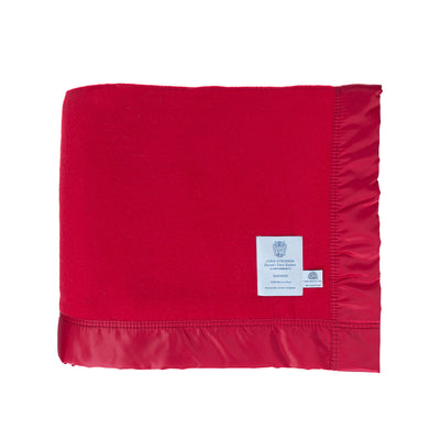 A cherry red Duchess Merino Wool Blanket by John Atkinson with satin binding, folded on a white background. Medium-weight blanket, warm, with traditional satin-style ribbon trim, with John Atkinson and Woolmark labels. From The Wool Company